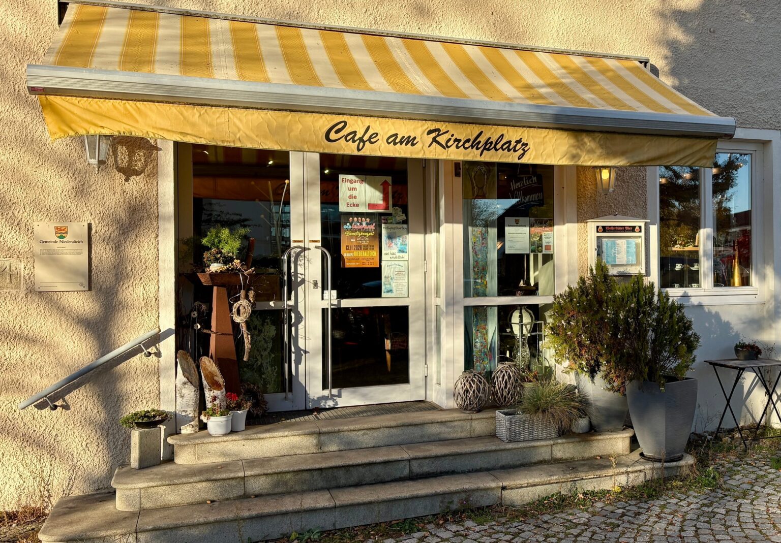 Eingang des Café am Kirchplatz mit gelb-weiß gestreifter Markise und Treppe