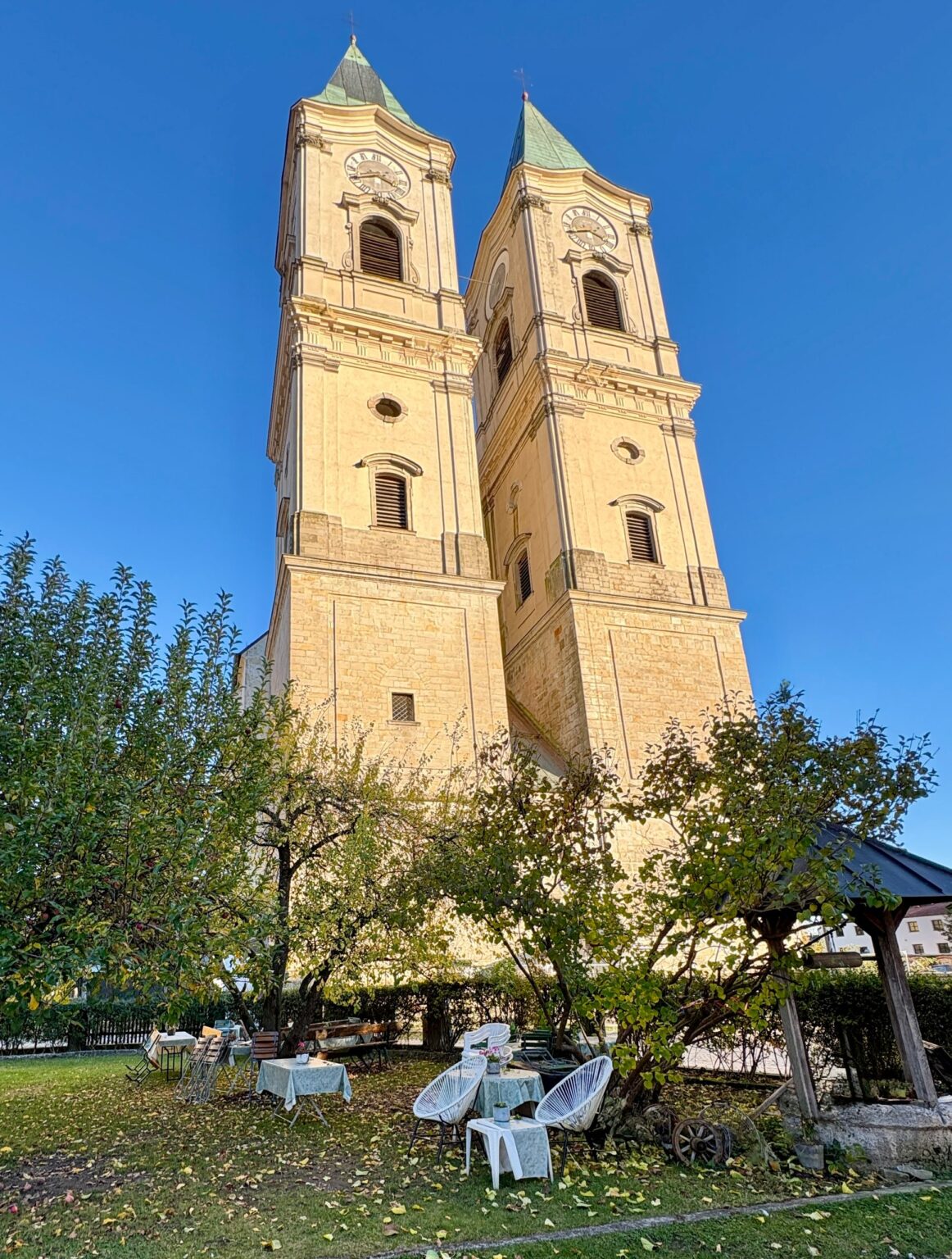 Garten des Café am Kirchplatz mit gedeckten Tischen unter Apfelbäumen, dahinter die Türme der Basilika Niederalteich